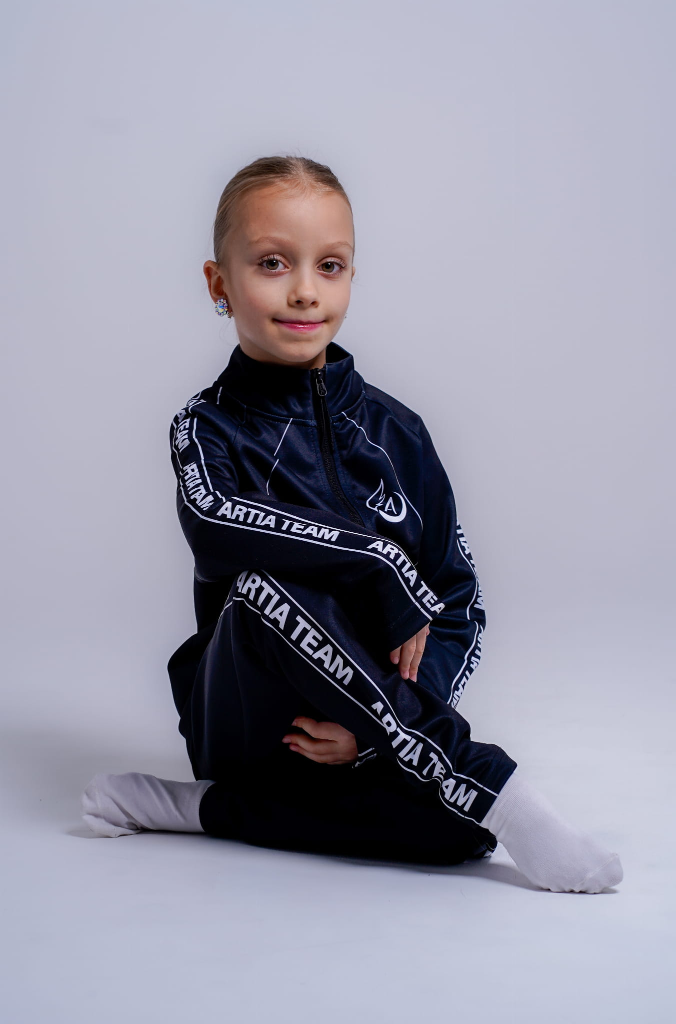 czarne dresowe spodnie  z białymi napisami artia team na boku.  prezentowane na modelce, która siedzi. widok z przodu.