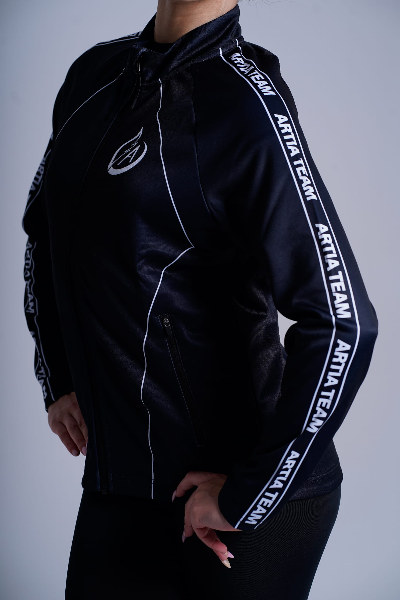 czarna dresowa bluza rozpinana  z białymi napisami artia team na boku oraz sygnet Artia na piersi.  prezentowane na modelce. widok z przodu, bliskie ujęcie na detale.